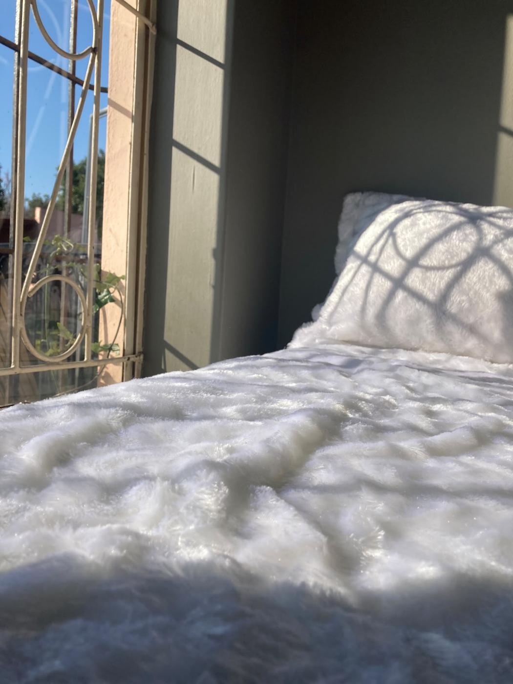 Close-up of textured white throw on a bed beside a window with light patterns