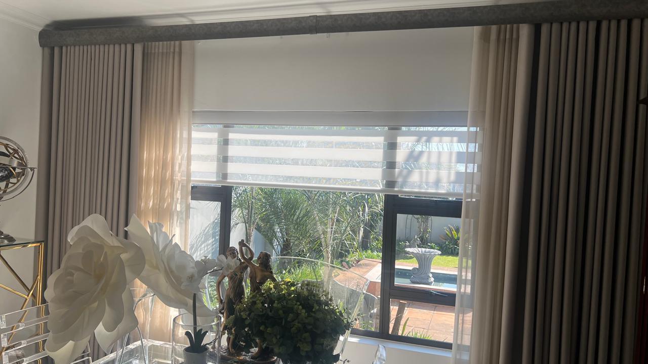 Sheer roman blind framed by wave-fold curtains, bay window