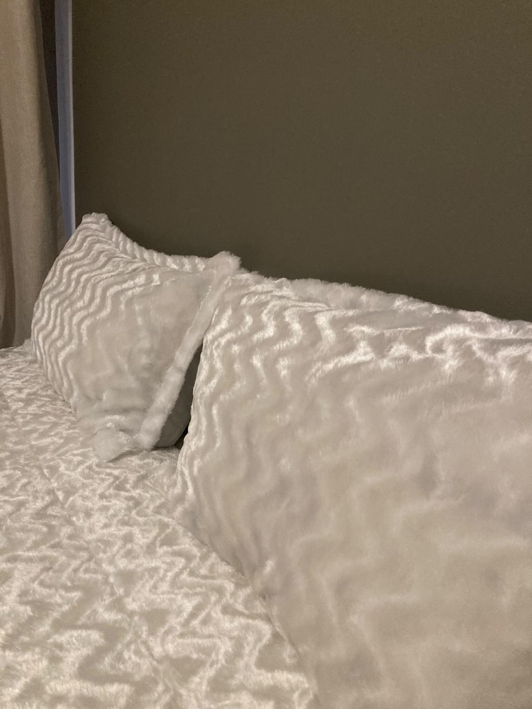 Textured white bedding with pillows against an olive headboard wall